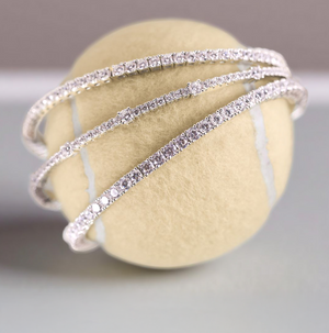 Lafonn simulated diamond tennis bangles in sterling silver, elegantly wrapped around a tennis ball, showcasing brilliant sparkle and timeless design.
