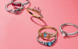 Disney x Pandora princess rings arranged on a vibrant pink backdrop.