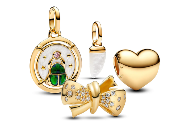 A collection of 14K gold-plated Pandora Charms, including the Be Love engravable heart charm, a sparkling bow charm, a Scarab beetle medallion charm, and a mini shark tooth charm.