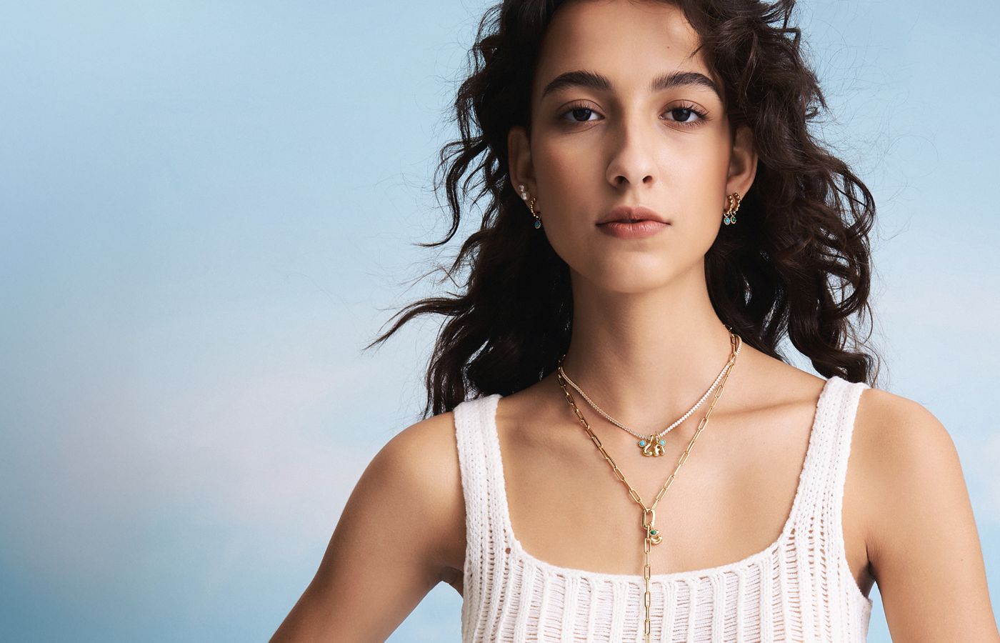 Fashionable girl showcasing teal and green charm hoop earrings, a sparkling diamond necklace with gold letter charms, and a statement lavaliere necklace.