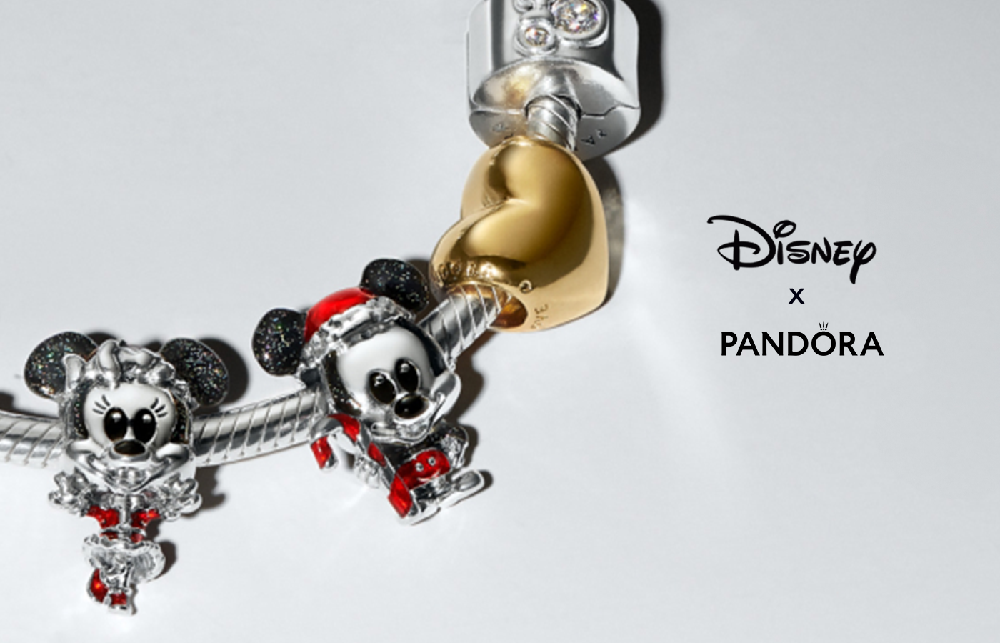 Close-up of Disney x Pandora holiday charm bracelet featuring festive Minnie and Mickey Mouse charms in red enamel with glitter accents, alongside a gold heart charm and silver pavé clasp — perfect for Disney fans and holiday gifting.